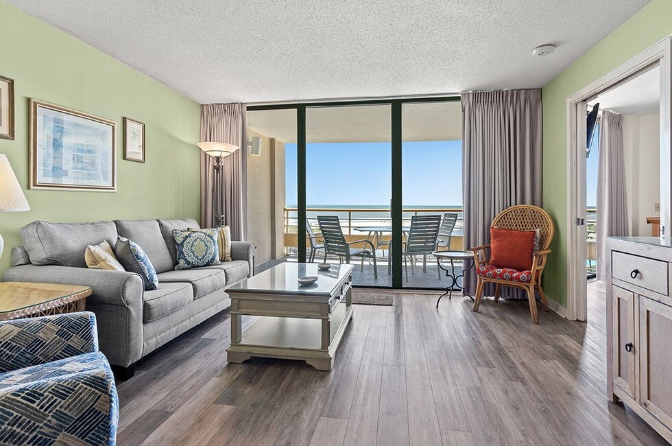 A wide view of a living room with a sofa, coffee table, and balcony overlooking the ocean.