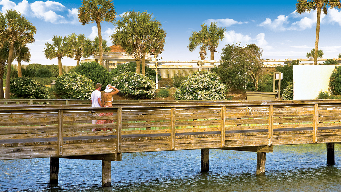 A wooden pier over water with a couple walking on it