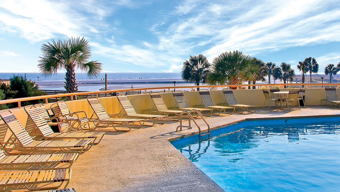 A serene poolside scene with lounge chairs, palm trees, and a view of the ocean.