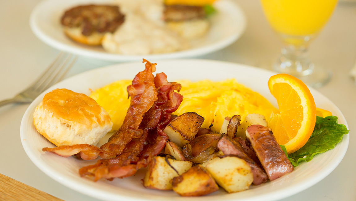 A plate of breakfast food with bacon, eggs, potatoes, and a biscuit.
