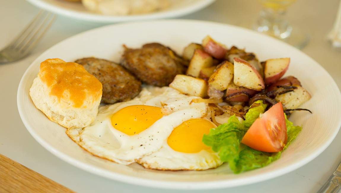 A plate of breakfast food with eggs, sausage, potatoes, and biscuit.