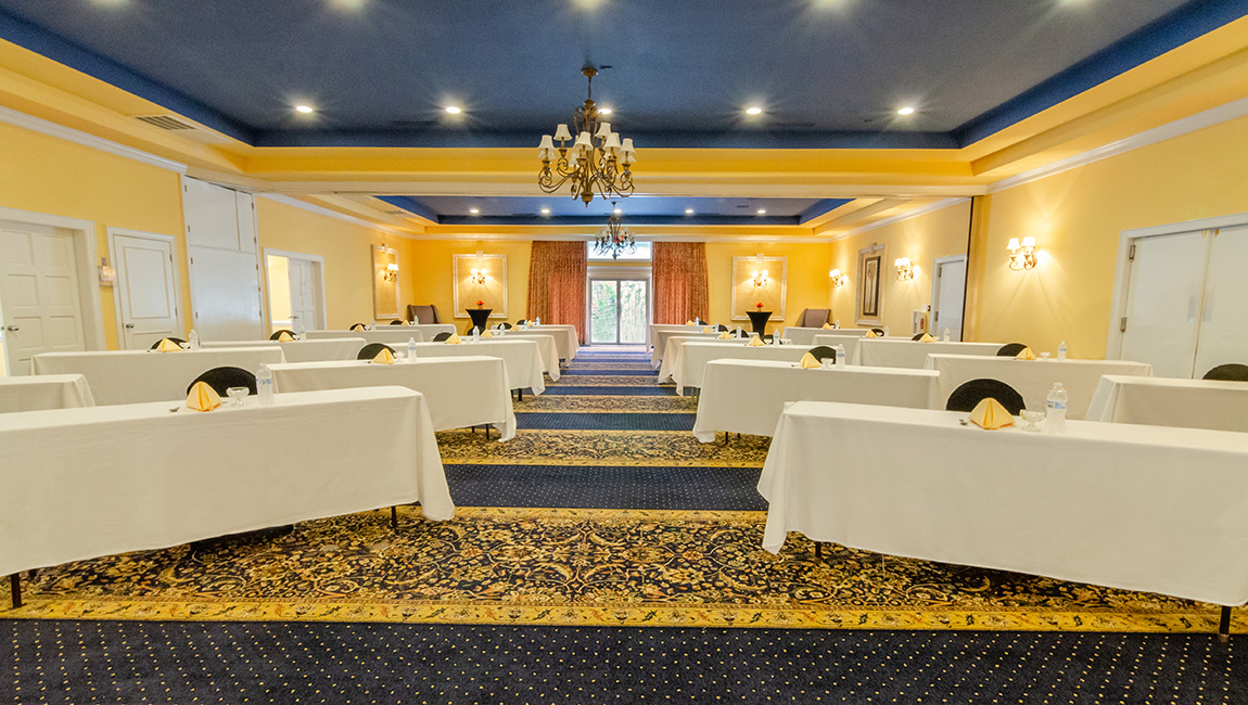 A wide view of a meeting room with yellow walls, blue ceiling, and white tables.