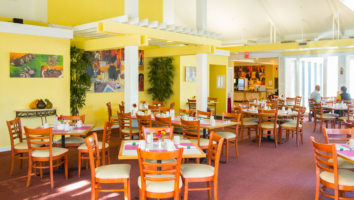 A brightly lit dining area with yellow walls, white beams, and wooden chairs.