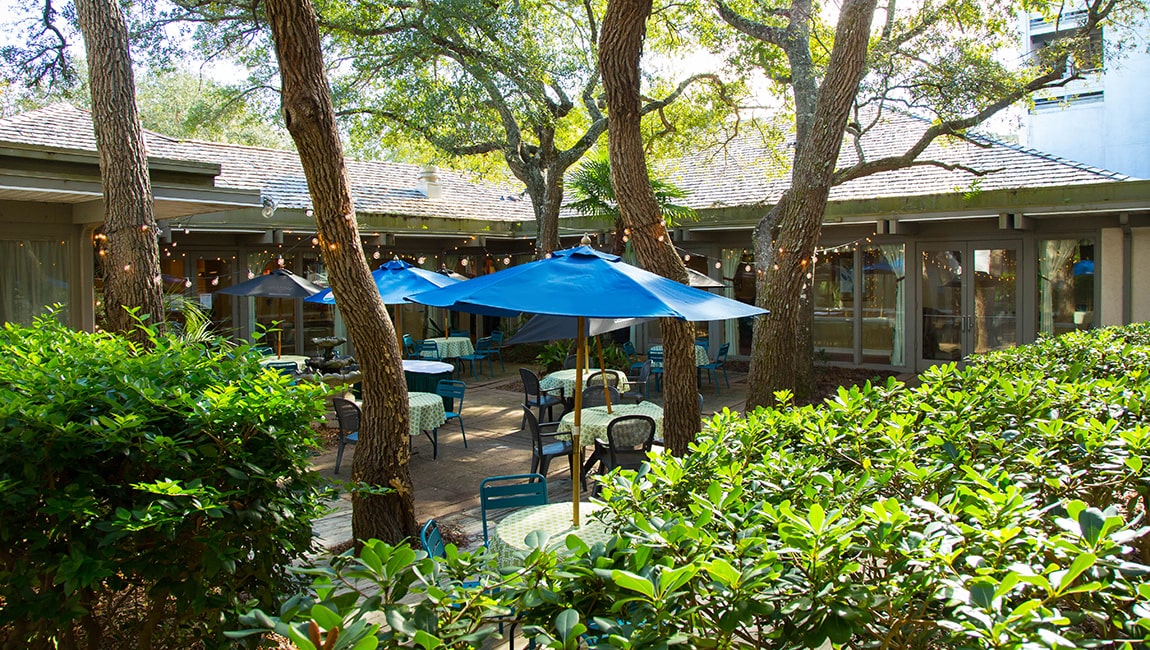 A courtyard with outdoor seating, blue umbrellas, and string lights.