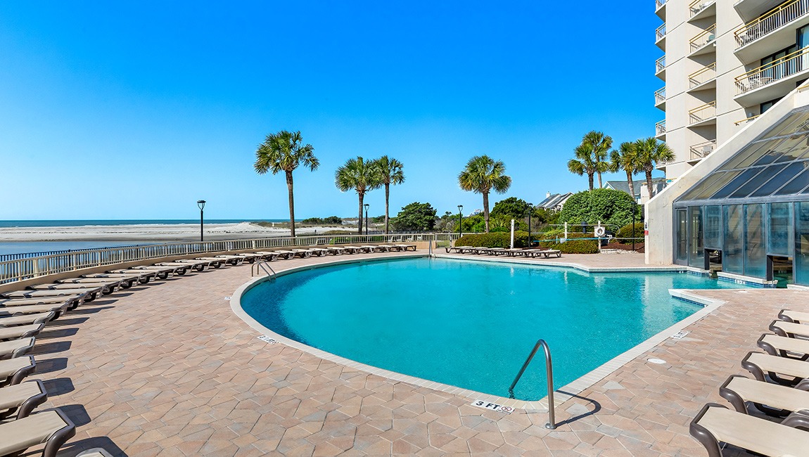 A large pool with a beach and palm trees in the background.