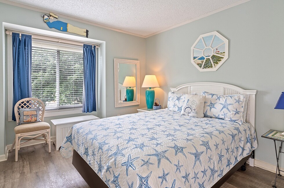 A wide view of a coastal-style bedroom with a blue and white color scheme, a starfish-patterned bedspread, and white furniture.