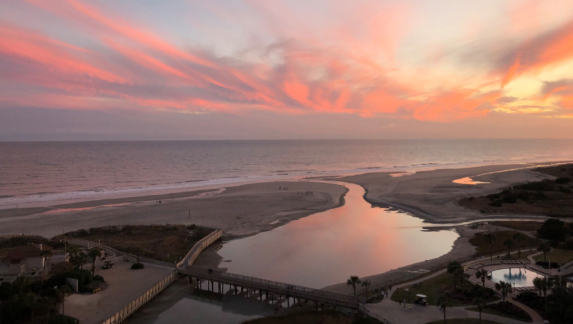 Aerial view of a beach at sunset with a pier and waterway.